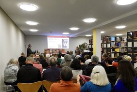 rund 30 sitzende Personen von hinten im Lesesaal des Stadtarchivs. Rechts Reihen von Bücherregalen. Vorne Stadtarchivar Engelhard, der eine Präsentation zeigt. 