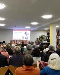 rund 30 sitzende Personen von hinten im Lesesaal des Stadtarchivs. Rechts Reihen von Bücherregalen. Vorne Stadtarchivar Engelhard, der eine Präsentation zeigt. 